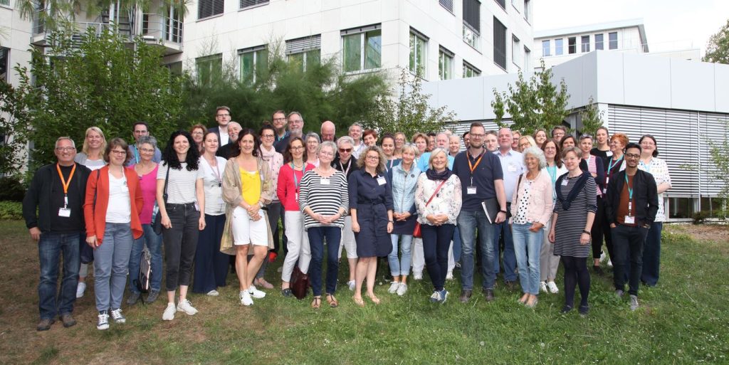 Gruppenfoto des Netzwerkpartnertreffens 2019 auf einer grünen Wiese. Im Hintergrund das Gebäude der Aktion Mensch in Bonn.